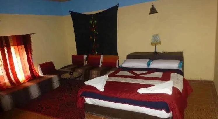 Hotel auberge Sahara room with double bed featuring red and white bedding, corner seating with cushions, and tasseled curtains