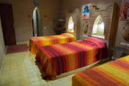 Hotel auberge Sahara bedroom with three single beds featuring striped orange, red, and yellow bedspreads in a rustic room