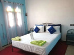 Hotel auberge Sahara bedroom with white bed linens, blue and white pillows, green towels, blue walls, and arched windows with white curtains