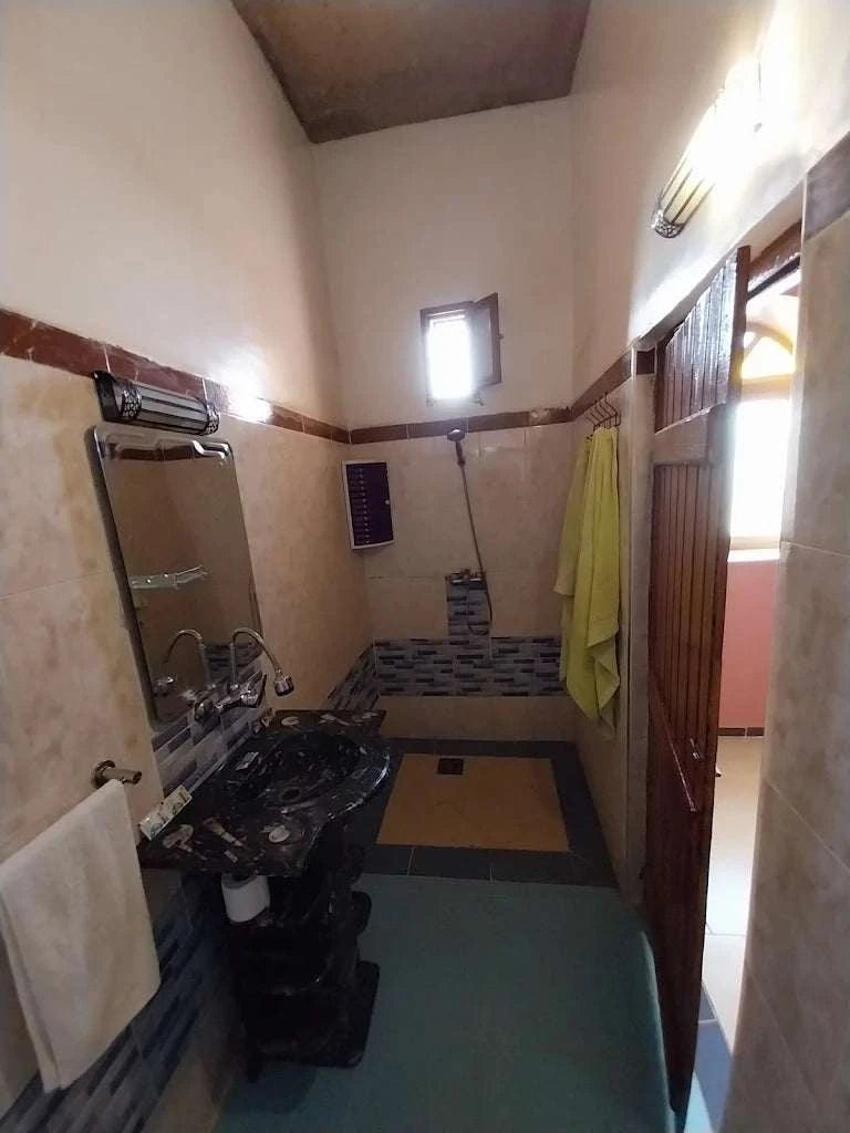 Hotel auberge Sahara bathroom with beige tiled walls, black marble sink, small window, and towel hanging on wall