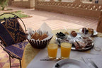 Breakfast setting at Hotel auberge Sahara with glasses of orange juice, bread basket, boiled egg, olives, jam bowls on a yellow tablecloth