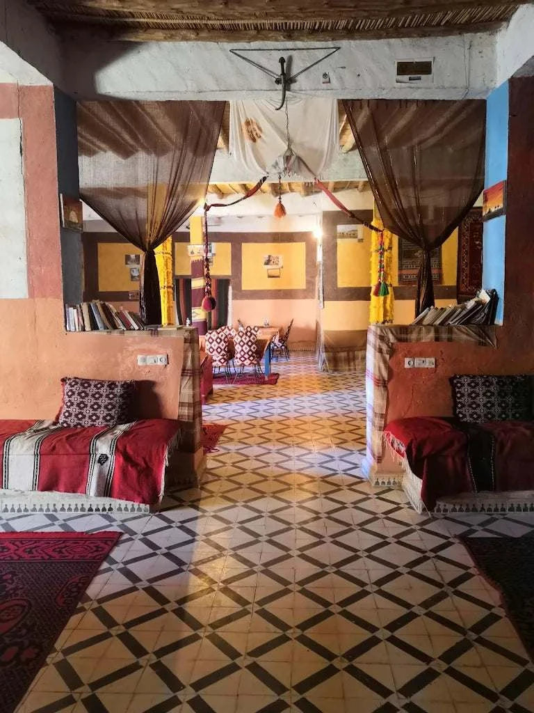 Hotel auberge Sahara cozy seating area with red cushions, patterned pillows, geometric tiled floor, and sheer brown curtains