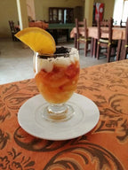 Dessert glass with orange slice and layered cream and fruit on an orange patterned tablecloth in Hotel auberge Sahara dining area