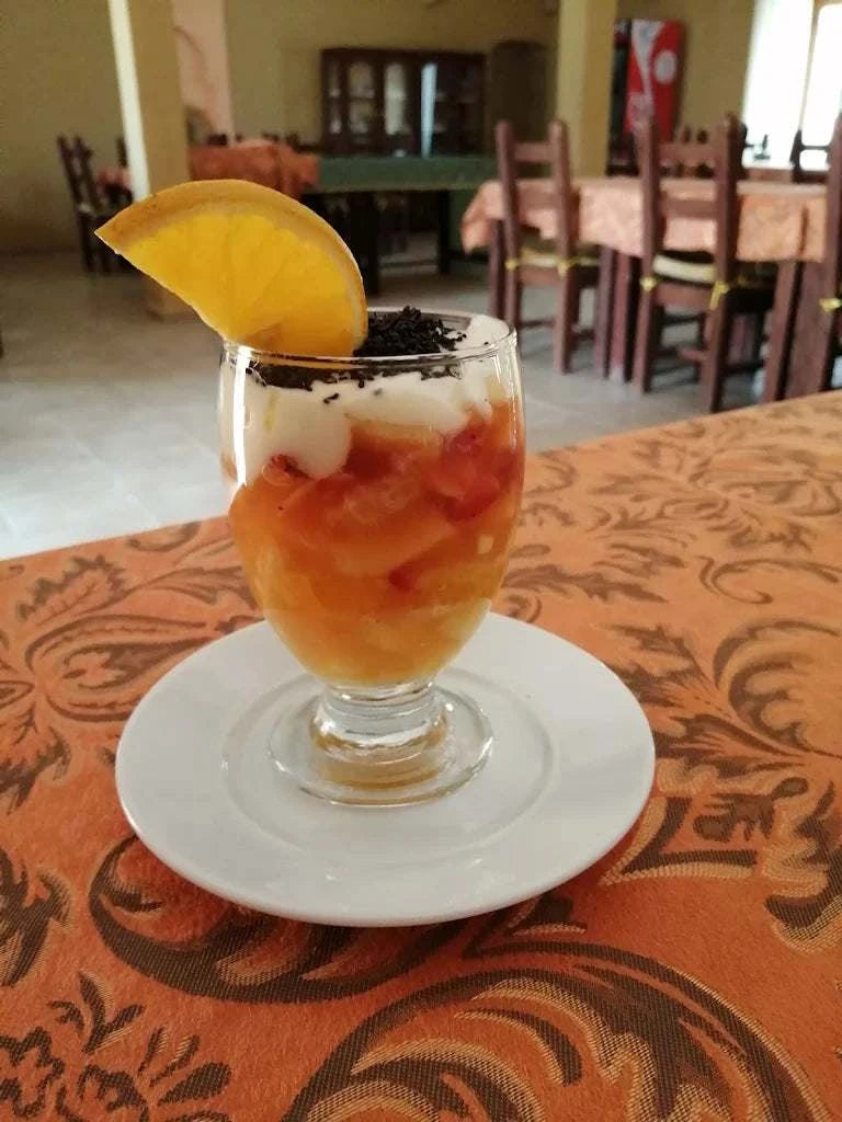 Dessert glass with orange slice and layered cream and fruit on an orange patterned tablecloth in Hotel auberge Sahara dining area