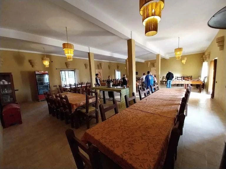 Hotel auberge Sahara dining room with long wooden tables covered in orange patterned tablecloths and wooden chairs under hanging lantern lights
