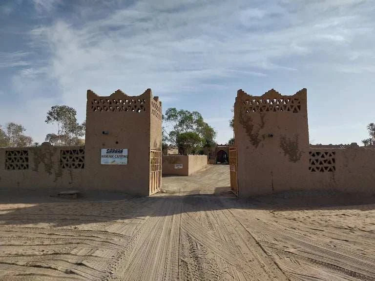 Hotel auberge Sahara entrance with traditional brown adobe walls and latticework towers under a cloudy sky