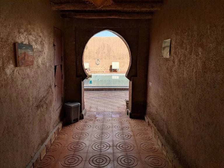 Hotel auberge Sahara courtyard with traditional Moroccan stucco archway, terracotta tiles with circular patterns, and a pool