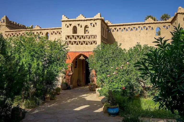 Hotel auberge Sahara with traditional beige mud-brick walls and decorative geometric patterns surrounded by greenery and potted plants