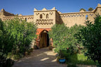 Hotel auberge Sahara with traditional beige mud-brick walls and decorative geometric patterns surrounded by greenery and potted plants
