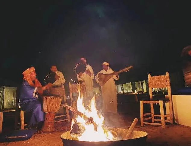 Hotel auberge Sahara nighttime scene with musicians in traditional Moroccan attire playing drums and string instruments around a campfire