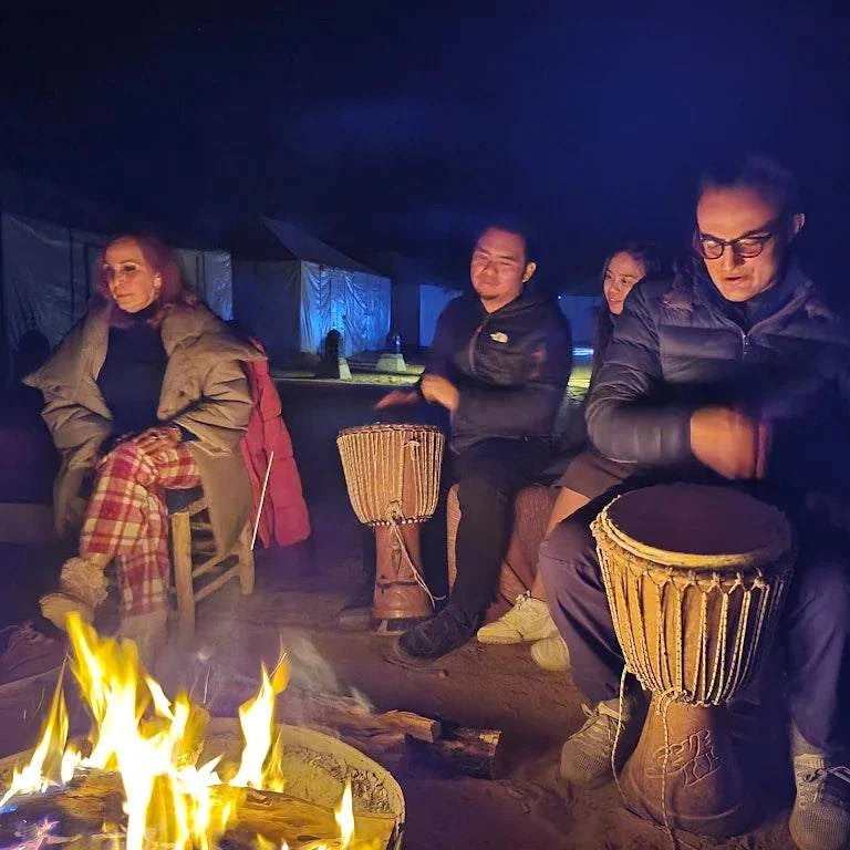 Hotel auberge Sahara nighttime scene with people sitting around a campfire playing traditional drums, tents in the background