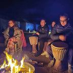 Hotel auberge Sahara nighttime scene with people sitting around a campfire playing traditional drums, tents in the background