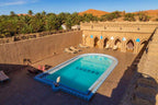 Hotel auberge Sahara outdoor swimming pool with blue water and tiled edge surrounded by terracotta walls and sun loungers