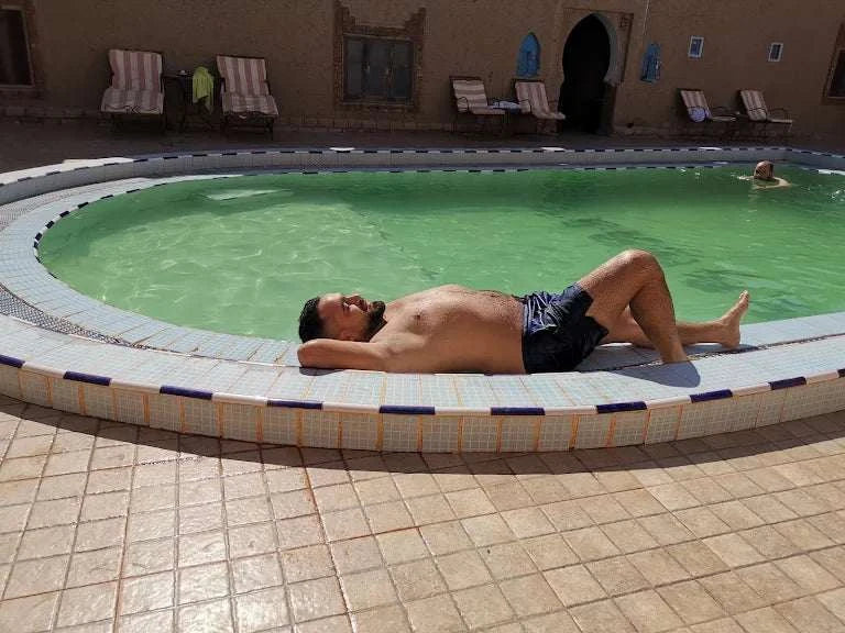 Hotel auberge Sahara outdoor round swimming pool with tiled edge and man sunbathing on poolside in black shorts