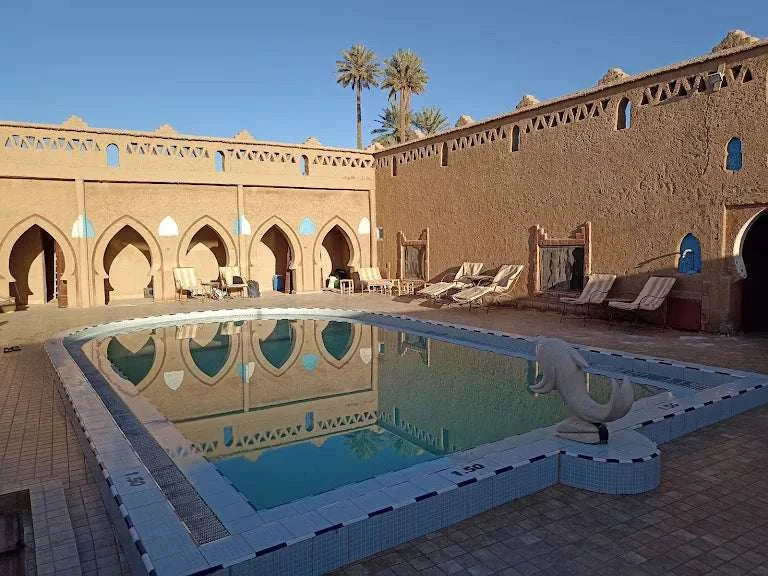 Hotel auberge Sahara outdoor swimming pool with light blue tiles, surrounded by beige adobe walls and palm trees