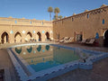 Hotel auberge Sahara outdoor swimming pool with light blue tiles, surrounded by beige adobe walls and palm trees