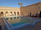Hotel auberge Sahara outdoor swimming pool with light blue tiles, surrounded by beige adobe walls and palm trees