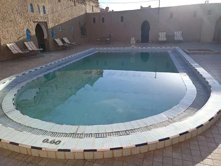 Hotel auberge Sahara outdoor swimming pool with tiled edge surrounded by sand-colored walls and lounge chairs