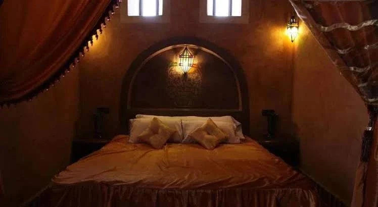 Hotel auberge Sahara room with warm lighting, beige bedding, decorative cushions, textured walls, and arch window detail