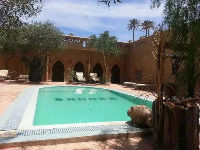 Hotel auberge Sahara outdoor turquoise swimming pool with brown Moroccan-style arches and palm trees surrounding it