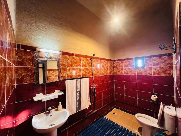Hotel Camping Les Roses bathroom with maroon and orange tiled walls, white sink, towel rack, toilet, and a small window