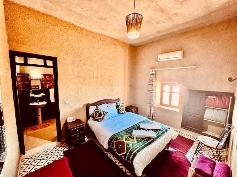 Hotel Camping Les Roses cozy bedroom with textured beige walls, patterned textiles, wooden furniture, and a window
