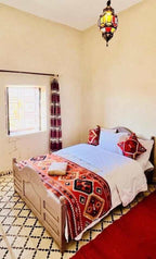 Hotel Camping Les Roses bedroom with wooden bed, white bedding, red and orange patterned blanket and pillows, tiled floor and decorative lantern