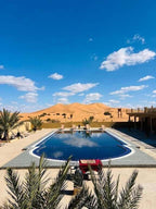Outdoor rectangular blue swimming pool with white tiles, surrounded by palm trees and desert dunes at Hotel Camping Les Roses
