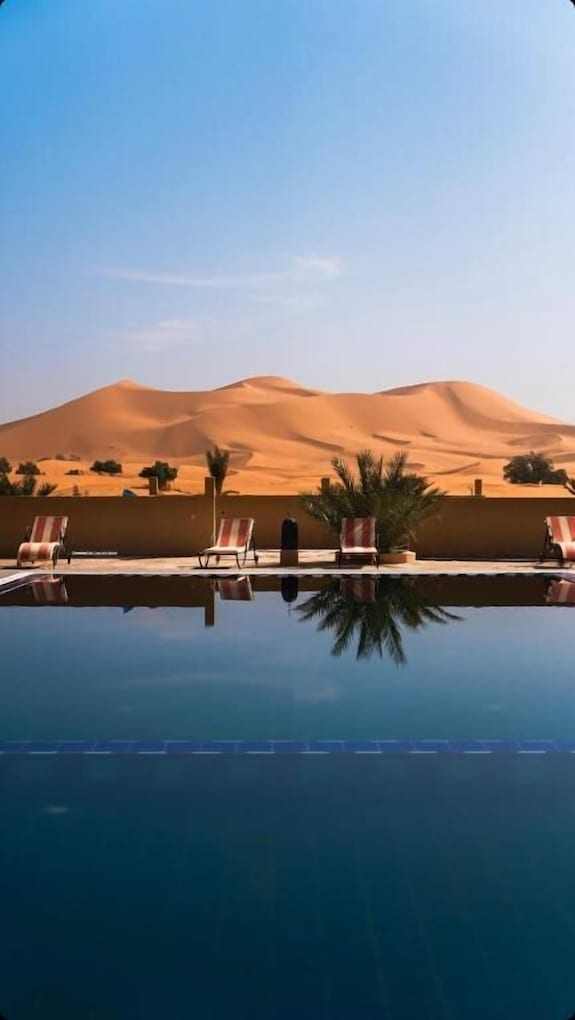 Hotel Camping Les Roses outdoor pool with clear blue water, surrounded by sun loungers and desert sand dunes in background