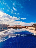 Hotel Camping Les Roses outdoor pool with clear blue water reflecting sky, surrounded by desert landscape and lounge chairs