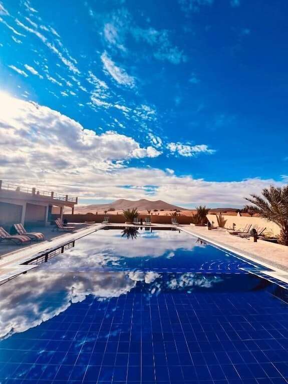 Hotel Camping Les Roses outdoor pool with clear blue water reflecting sky, surrounded by desert landscape and lounge chairs