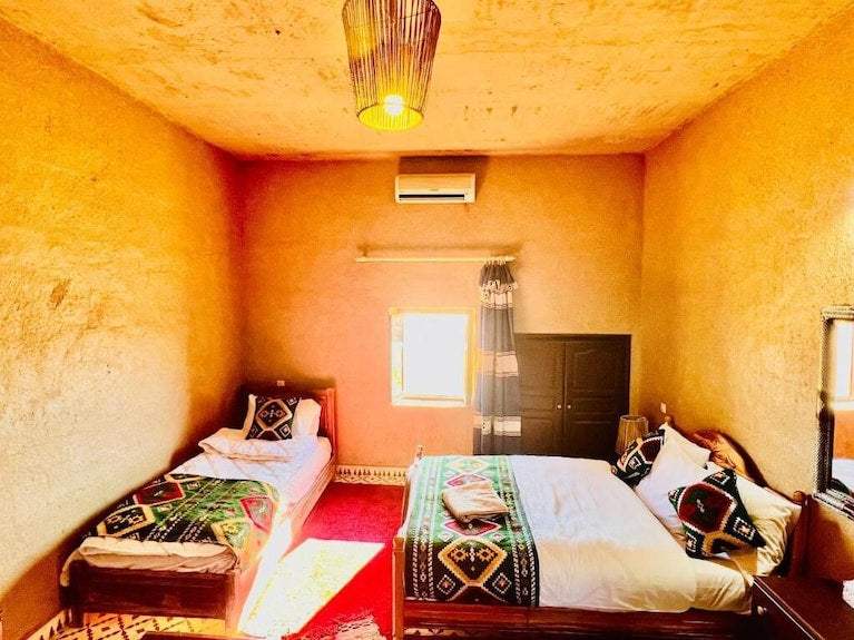 Hotel Camping Les Roses room with textured warm beige walls, twin and double beds featuring colorful geometric patterned bedding, a wooden wardrobe, and a hanging lamp
