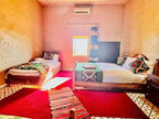 Hotel Camping Les Roses bright room with two wooden beds, colorful patterned bed runners and cushions, red carpet, and beige walls