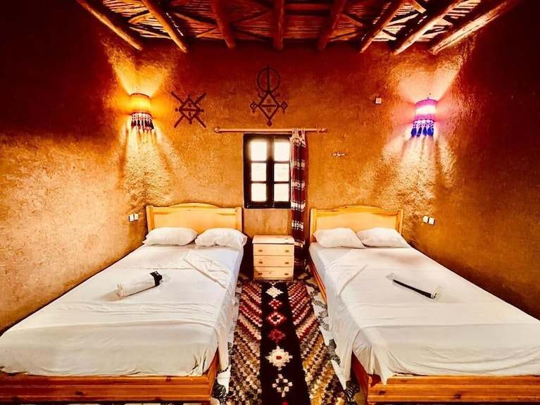Hotel Camping Les Roses twin wooden beds with white linens in a rustic room featuring earth-toned walls and decorative wall sconces