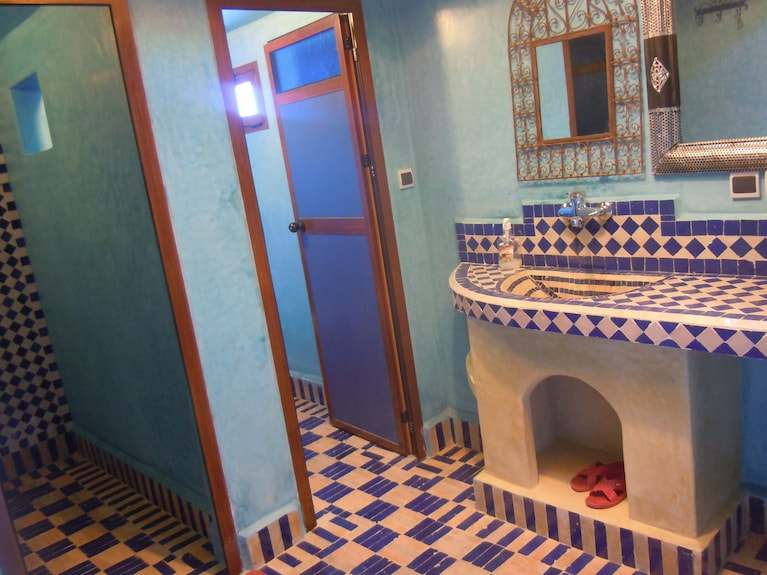 Hotel Kasbah Ksar Bicha bathroom with blue and white geometric tiled sink and floor, wooden doors, and blue textured walls