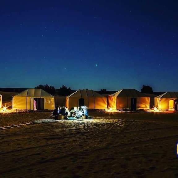 Hotel Kasbah Ksar Bicha beige desert tents illuminated at night with group of people sitting on sandy ground under starry sky