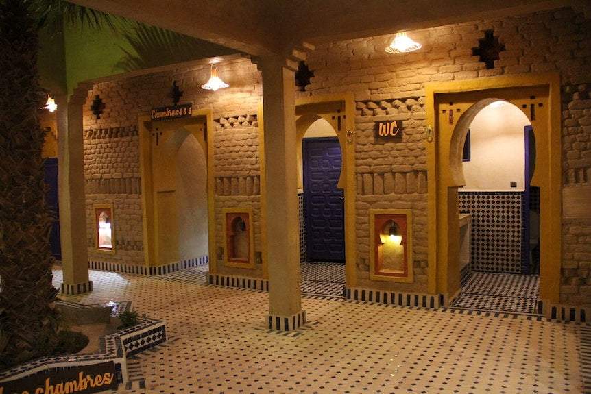 Hotel Kasbah Ksar Bicha traditional Moroccan kasbah-style architecture interior with yellow and brown adobe walls, arches, columns, and tiled black and white patterned floor