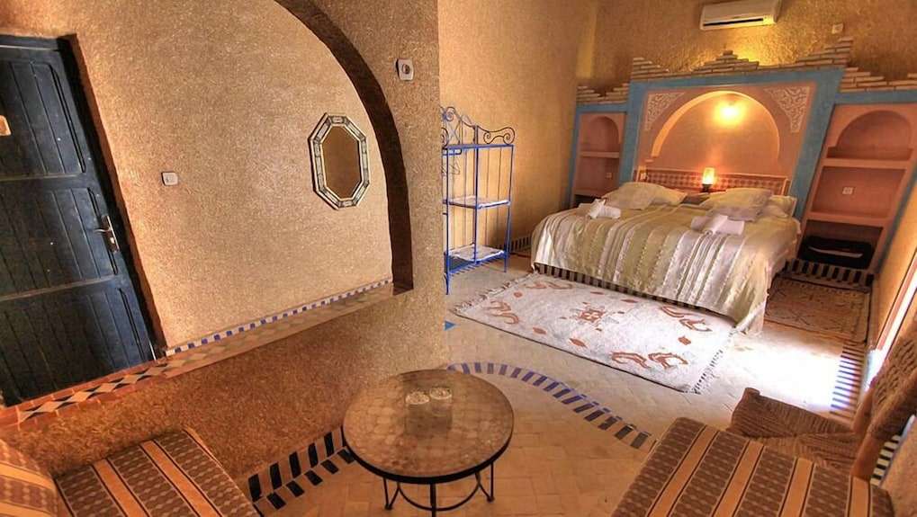 Hotel Kasbah Ksar Bicha bedroom with Moroccan style decor featuring a double bed, patterned rug, archway, and textured walls