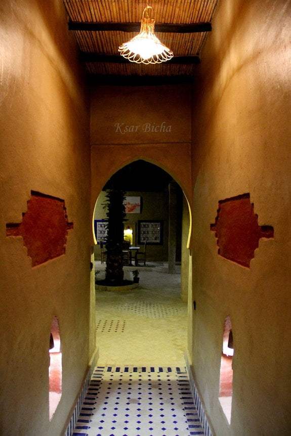 Hotel Kasbah Ksar Bicha narrow Moroccan-style corridor with earthy brown walls, arched doorway, and decorative cutouts