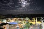 Hotel Kasbah Ksar Bicha at night with illuminated pool, palm trees, and traditional Moroccan kasbah architecture under a cloudy moonlit sky