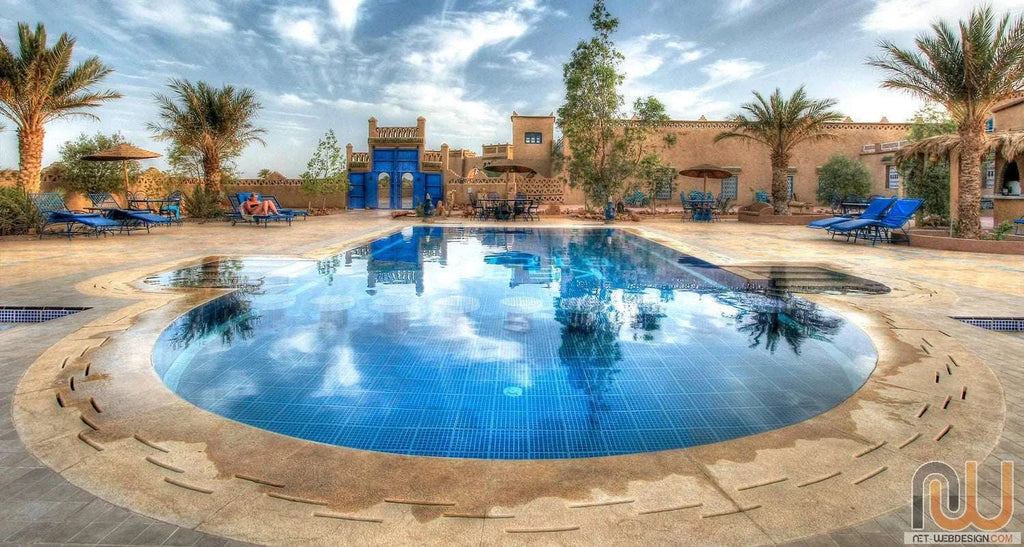 Hotel Kasbah Ksar Bicha outdoor swimming pool with blue lounge chairs, palm trees, and traditional Moroccan kasbah architecture