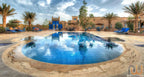 Hotel Kasbah Ksar Bicha outdoor swimming pool with blue lounge chairs, palm trees, and traditional Moroccan kasbah architecture