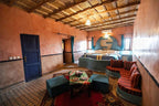 Hotel Kasbah Ksar Bicha room with warm terracotta walls, traditional wooden ceiling, teal sofa and stools, patterned rugs, and round bed