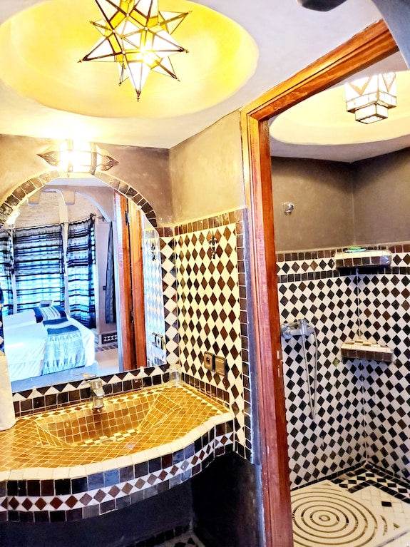 Hotel Ksar Merzouga bathroom with brown and white intricate mosaic tiles, a star-shaped ceiling light, and a wooden framed mirror