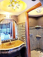 Hotel Ksar Merzouga bathroom with brown and white intricate mosaic tiles, a star-shaped ceiling light, and a wooden framed mirror