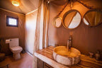 Hotel Ksar Merzouga bathroom with beige fabric walls, stone sink, wooden countertop, three round mirrors, and white toilet