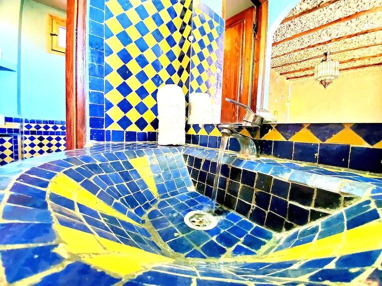 Hotel Ksar Merzouga bathroom sink with blue and yellow geometric patterned ceramic tiles and a modern faucet