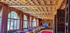 Hotel Ksar Merzouga dining room with wooden ceiling, large arched windows, and tables covered in yellow and purple tablecloths