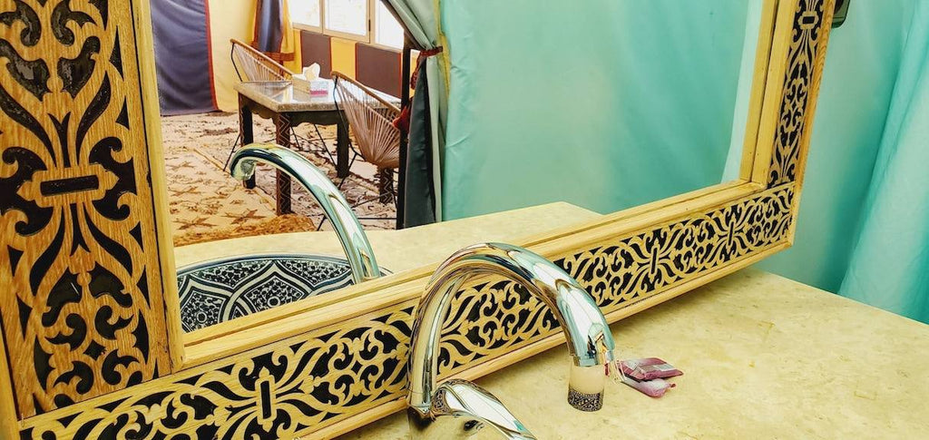 Hotel Ksar Merzouga featuring an ornate wooden framed mirror with intricate carvings above a beige marble countertop and chrome faucet