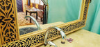 Hotel Ksar Merzouga featuring an ornate wooden framed mirror with intricate carvings above a beige marble countertop and chrome faucet